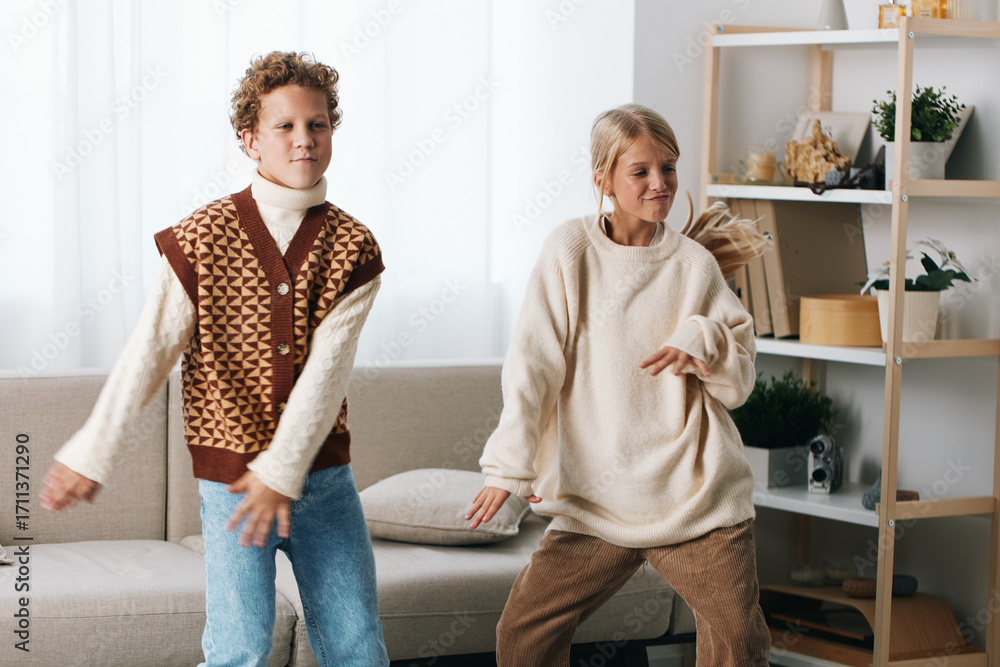 Fototapeta premium Authentic scene of playful movement at home, featuring a school aged child and adult dancing, casual knitwear, candid moment, wholesome lifestyle.