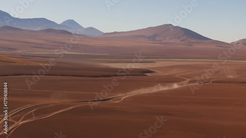 Aerial shot of a car driving through a scenic road in the Atacama highlands surrounded by mountains and volcanoes under the summer sun in one of the most remote landscapes in Chile
