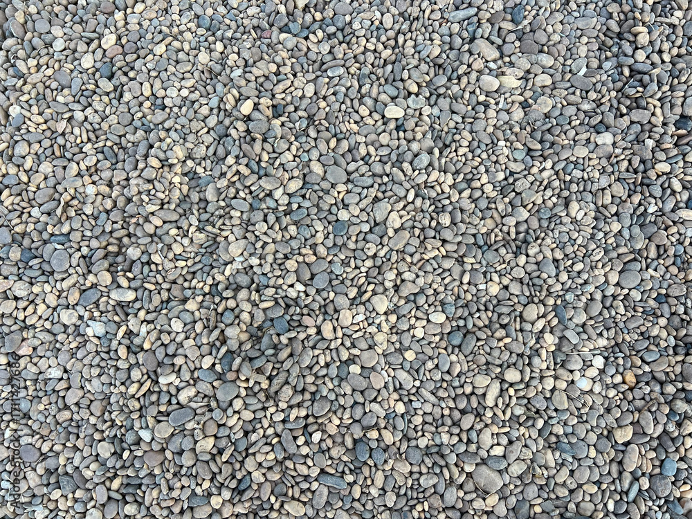 Obraz premium A close-up, top-down view of a collection of small, smooth river stones or pebbles. The stones vary in color, primarily featuring shades of gray, tan, and brown.
