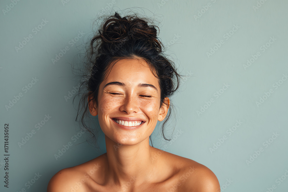 Obraz premium A young woman with a messy bun smiling with her eyes closed, showcasing a joyful and relaxed expression.