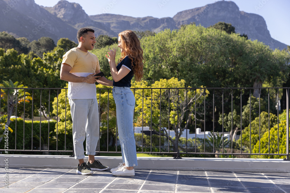 Fototapeta premium Young couple enjoying conversation on sunny balcony with scenic mountain view