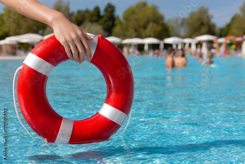 Hand holding red lifebuoy in swimming pool on sunny day