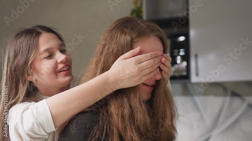 Wallpaper Mural Buddy in kitchen as friend covers eyes playfully then releases both laugh warm candid moment soft daylight on hair casual home scene hands over face joyful surprise domestic fun genuine reaction Torontodigital.ca