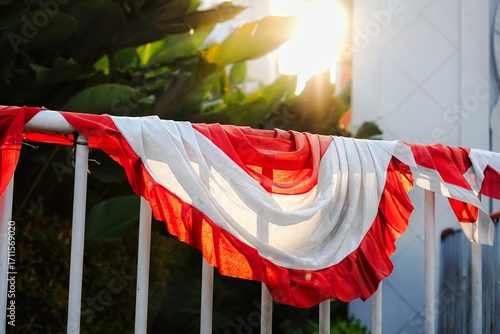 Festive red and white Indonesian banner, illuminated by bright sunlight, draped on a railing.
