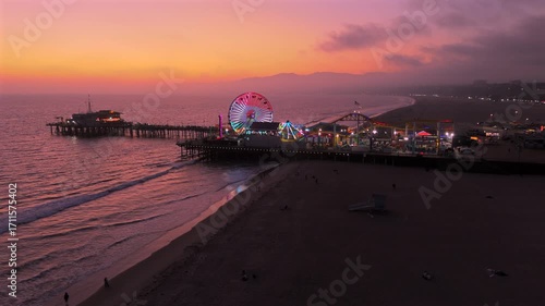 Breathtaking aerial sunset shot showcasing the iconic Santa Monica Pier in Los Angeles, beach, and Ferris wheel, reflecting stunning and vibrant colors as the day turns to night