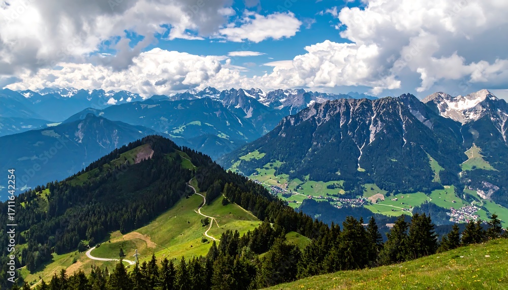 Obraz premium Panoramic vista of a mountain range with lush valleys, winding paths, and snow-capped peaks under a partly cloudy sky.