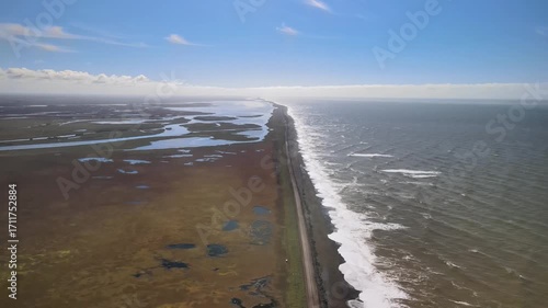 A long road stretches along the coastline of Cape Levashov, Kamchatka. On one side waves of the Sea of Okhotsk, on the other – numerous lakes, with clouds on the horizon.