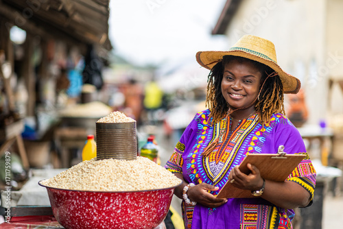 Portrait of Local African traditional woman entrepreneur, small business owner, SME, holding a clipboard at her outdoor market stall.