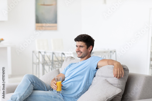 Handsome young man sitting on the sofa in the living room with juice, relaxing