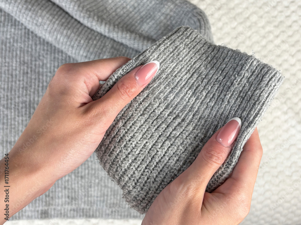 Obraz premium A woman holds the sleeve of a warm gray sweater with bobbles, checking fabric pilling. Preparing and caring for clothes, wardrobe organization for autumn and winter fashion seasons