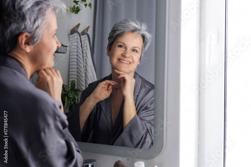 Mature beautiful woman in age during menopause with gray hair does self-care, facial massage