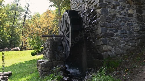Old stone watermill with a wooden water wheel in motion.