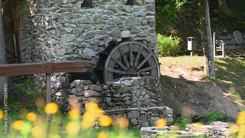 Old stone watermill with a wooden water wheel in motion.