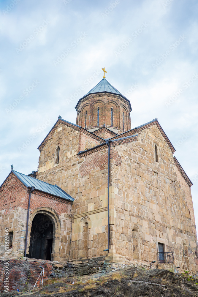 Fototapeta premium Close-up view of an ancient Georgian Orthodox stone church in Tbilisi, Georgia. With its detailed brickwork, arched entrance, cross-topped dome, the historic structure and spiritual heritage