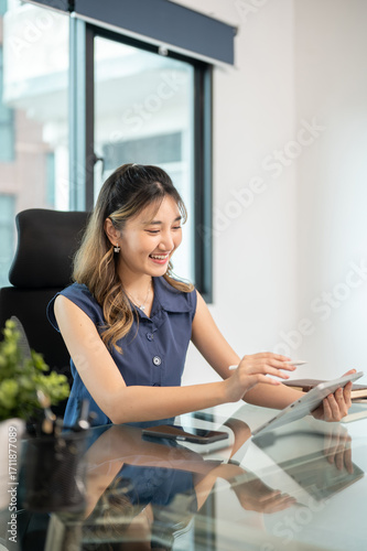 Asian woman office worker holding stylus and looking at tablet while sits at glass table in office. Free Download Asian woman office worker holding stylus and looking at tablet while sits at glass table in office. - GFXLoad