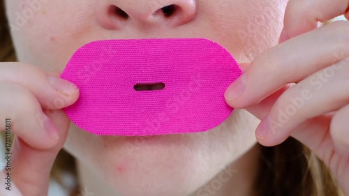 A girl puts a snoring patch on her mouth, close-up to sleep with her mouth closed and breathe through her nose. Healthy sound sleep with proper breathing. The toned oval of the face. Wellness