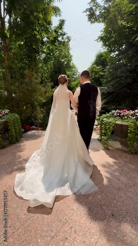 A beautiful wedding video. Happy newlyweds walk along a road in a park.