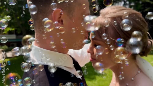 A beautiful wedding video. The happy newlyweds take photos in a park with soap bubbles.