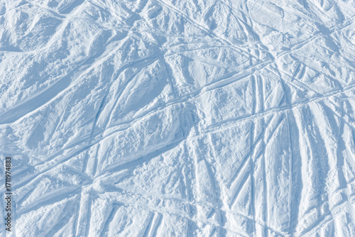 Snowy abstract off-piste skiing background with ski and snowboard trails and tracks on new virgin powder snow. morning sunrise or evening sunset time at alpine mountain resort