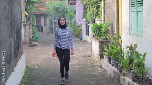 Asian Muslim Woman Walking Outdoors with Water Bottle in Indonesia