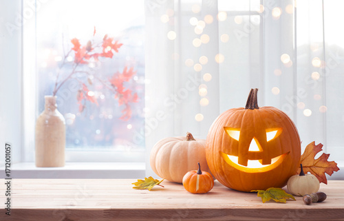 Background concept of traditional Halloween house decor with jack o lantern pumpkin on wooden table with copy space over blurred window