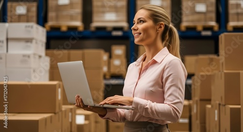 Woman with laptop in warehouse aisle surrounded by boxes checking inventory and stock levels