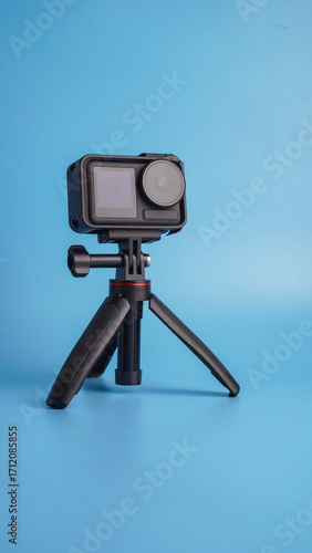 Action camera stands on a mini tripod, isolated on light blue background