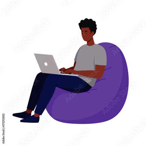 A young man with dark skin sits comfortably in a purple beanbag chair while working on a silver laptop.