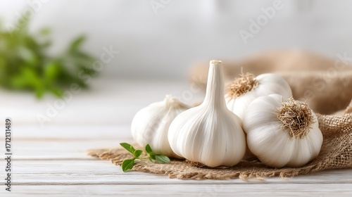 Fresh Garlic Bulbs on Burlap with Green Herb Leaf, White Wooden Tabletop Background