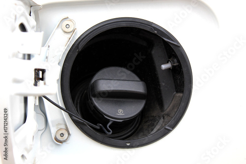 Macro shot of a black diesel fuel cap inside a white vehicle's fuel port. The plastic cap is securely closed, surrounded by a circular black housing with a tether for attachment.