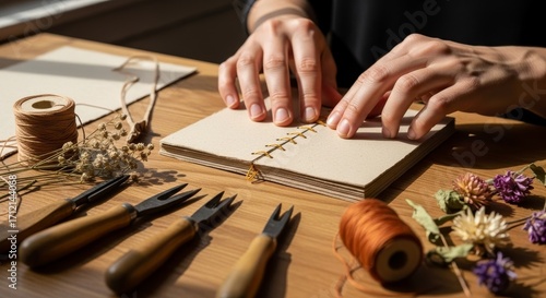 Hands crafting handmade book with bookbinding tools and dried flowers