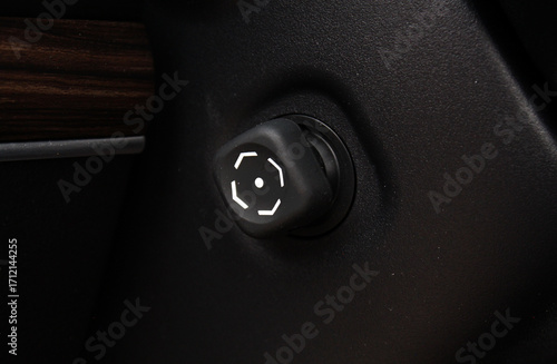 Close-up of a black plastic car seat adjustment knob with white circular markings, mounted on textured dashboard surface with wood trim detail visible on the side.