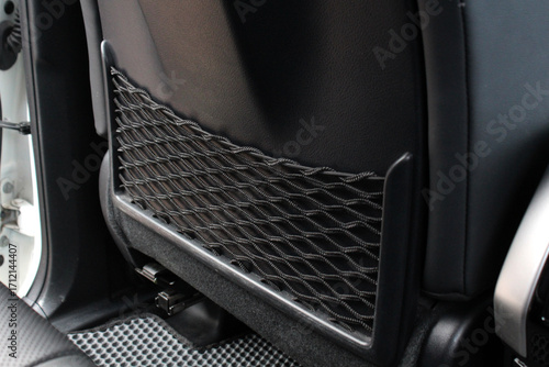 Close-up of a black car seatback storage pocket with elastic net, mounted on leather upholstery, designed for holding small items, combining practicality and modern automotive interior detail.