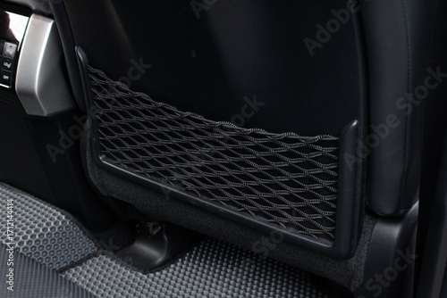 Close-up of a black car seatback storage pocket with elastic net, mounted on leather upholstery, designed for holding small items, combining practicality and modern automotive interior detail.