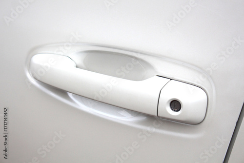White car door handle with integrated keyhole, smooth glossy finish, rounded ergonomic shape, mounted on metallic vehicle body, simple modern design and clean automotive detail.