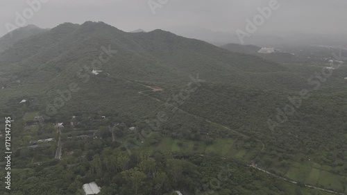Aerial drone shot of Kalika Mata Temple in Udaipur, Rajasthan, perched on a lush green mountain during a misty monsoon morning, surrounded by scenic Aravalli hills and natural greenery.