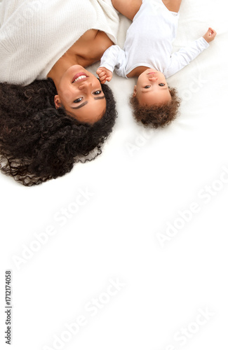 Happy young mother with curly hair lying on bed with her cute baby. Smiling family portrait, love, motherhood, childhood, care and bonding. Perfect image for parenting, lifestyle, and family concept.