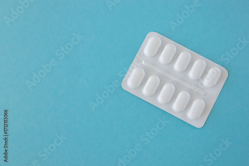 Tabletts or pills in white package on the blue paper background.