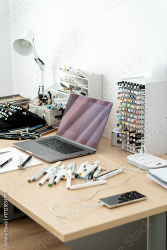 Close-up view of tidy home office desk with laptop, sketchbooks, and colorful art markers, symbolizing creative freelance work and remote profession.  
