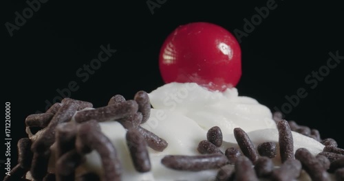 A chocolate frosted cupcake with sprinkles on top and a red cherry on top