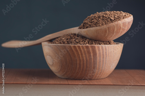 Instant coffee in a wooden bowl with a wooden spoon with coffee on a dark green background.