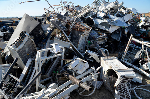 A large pile of scrapped metal, including many air conditioning units, at a junkyard. The image highlights the recycling process for electronic and appliance waste.
