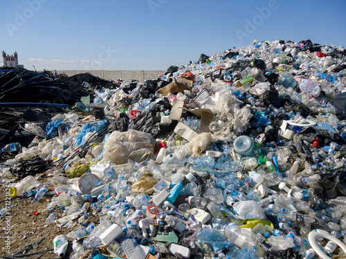 A massive pile of plastic bottles, containers, and household waste overflows a landfill. The image highlights a serious global issue of environmental pollution and overconsumption.