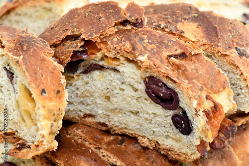 A close-up of a freshly baked olive bread from Cyprus. The rustic, homemade loaf is sliced to show the delicious black olives and herbs embedded within the dough.