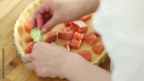 Woman fills a baking dish with fish and broccoli, preparing a healthy homemade quiche or casserole