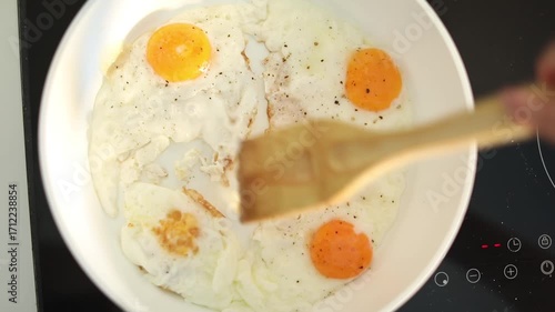 A woman fries fresh eggs in a skillet on her home kitchen stove, preparing a simple and delicious breakfast