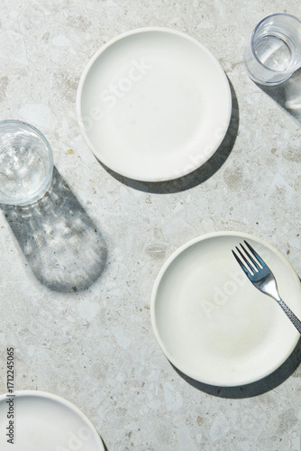 empty white plates on a grey terrazzo background with transparent glasses and a fork