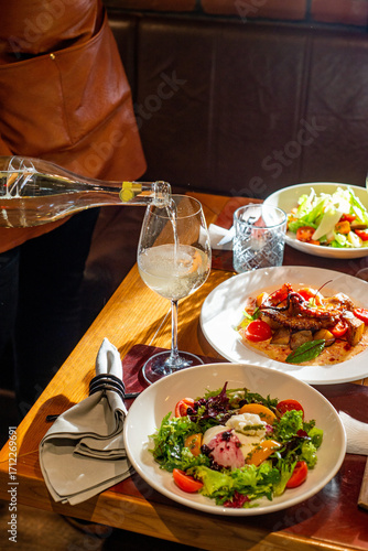 Unrecognizable Waiter pours wine into a glass on a table served with food in a restaurant
