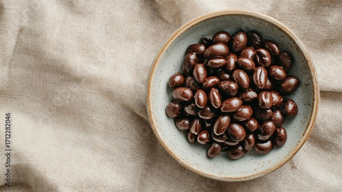 A minimalist top view of chocolate-covered espresso beans in ceramic bowl, tan linen backdrop