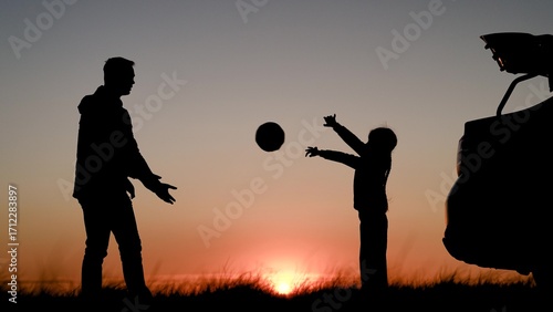 Happy dad kid playing with ball in nature near car. Parent child daughter stopped at camping by car. Family traveling by car dad child girl. Father child girl travel by car, play on field, sunset sky